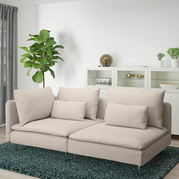 Minimalist living room with beige SÖDERHAMN sofa, green rug, plant, and white cabinet.