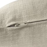Close-up of a zipper on a soft, textured, beige upholstered cushion.
