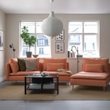 Bright orange iqö sofa sets in modern living room with large windows. Two sofas, coffee table, potted plant, and large hanging lamp.