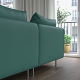 A teal sofa with metal legs near a window, offering deep seating and comfort.