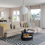 Modern living room with beige SÖDERHAMN sofa, striped rug, and large pendant lamp. Yellow pillows on couch, large window, and black coffee table.