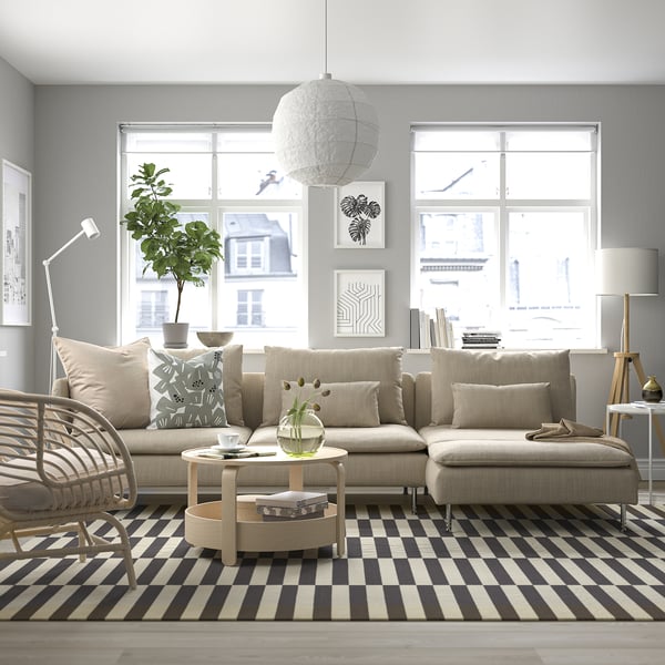 Modern gray SÖDERHAMN sectional, beige pillows, wooden coffee table, striped rug, floor lamp, large windows, city view. Relaxing, airy living room.