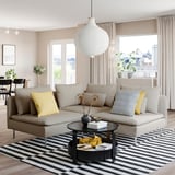 Modern living room with beige SÖDERHAMN sofa, black coffee table, striped rug, yellow pillows, large windows, and hanging light fixture.
