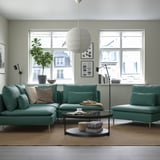 Modern living room with turquoise sectional sofa, light green walls, and large windows.