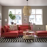Modern room with red SÖDERHAMN sectional, large windows, black/white checkered rug, wooden coffee table. Cozy, vibrant design.