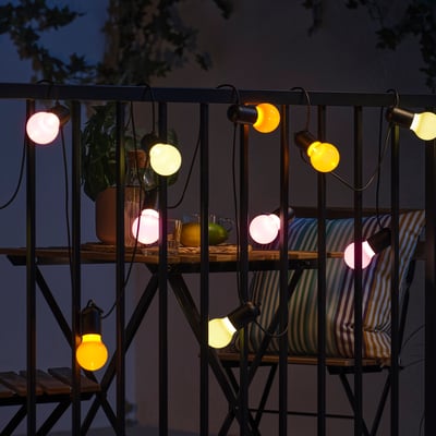 Colorful outdoor string lights, SOLVINDEN, with pink, yellow, and orange bulbs, connected by black wires, creating a warm and inviting atmosphere.