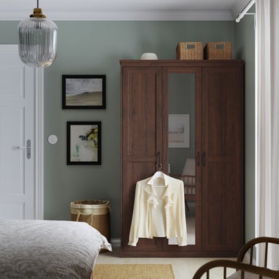 Bedroom with dark brown SONGESAND mirrored wardrobe, greenish walls, light carpet, and art.