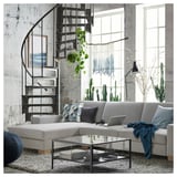 Modern living room with white SÖRVALLEN sofa, glass coffee table, metal spiral staircase, and large windows with cacti.