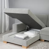 Modern sofa with storage ottoman open, showing blankets inside. Light grey fabric, wooden legs.