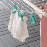SPACKLA green plastic pegs hold white socks on drying rack, small, bright, organized.