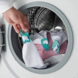 Person placing socks, attached to teal SPACKLA clips, into a washing machine.