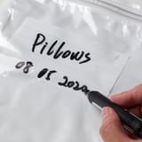 Hand writes pillows 08/01/2020 on bag, showcasing SPANTAD storage bags usage for labeling and organizing.