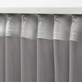 Gray sheer curtains with metal hooks hanging, diffusing daylight, ideal for layered window treatments.