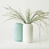 Two modern vases, light blue and white, cylindrical with vertical ridges, holding dried grasses.