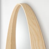 Arched wooden-framed mirror with light ash veneer hangs against a plain wall, showcasing its sleek, streamlined design.