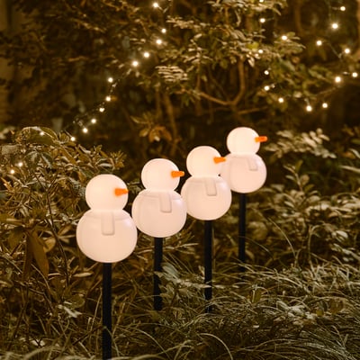 Four snowman-shaped decorations light up, casting a warm glow in a garden bed, creating a festive atmosphere at night.
