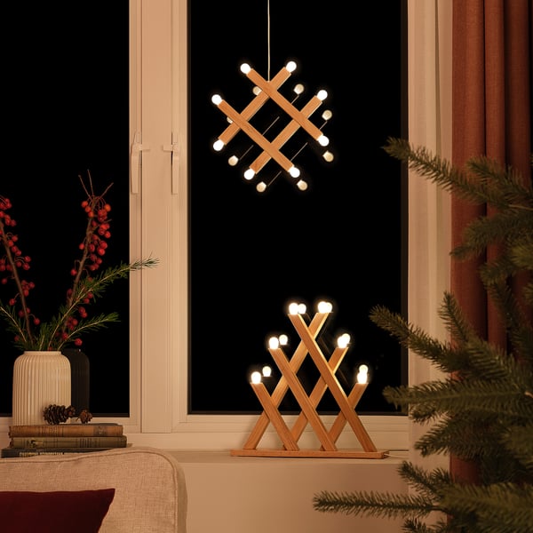 Cozy pine pendant and table lamp duo, battery-operated, emitting warm white light, sitting on a window sill beside a christmas tree.