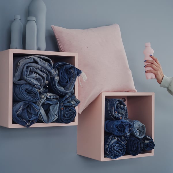 Pink fabric bins hold neatly folded jeans; blue wall background.