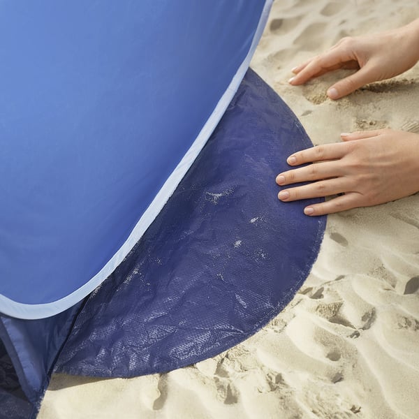 Person holding blue sun shelter, featuring mesh for airflow on sandy beach.