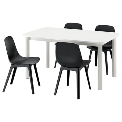 A white IKEA STRANDTORP extendable dining table with four black chairs. The chairs have curved seats and black legs.