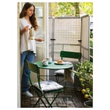 Woman pours coffee on small balcony with green SUNDSÖ furniture set.