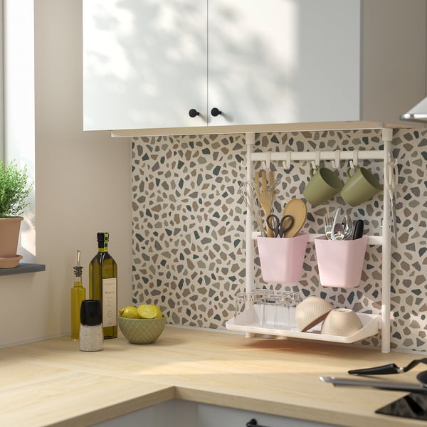 Modern kitchen with SUNNERSTA rack holding pink containers and green mugs, lemons, olive oil, and seasonings nearby.
