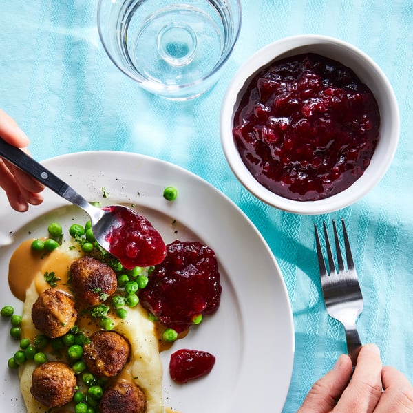 Meal with meatballs, peas, mashed potatoes, jam, spoon, fork, bowl, blue tablecloth