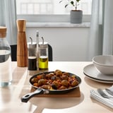 Cooked meal in black frying pan on wooden table. Condiments nearby.