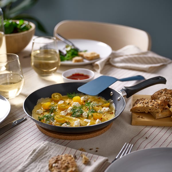 Breakfast setup with gray frying pan, yellow dish, plates, bread, glasses, and salad bowl.