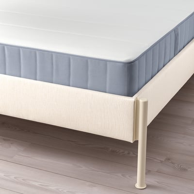 A TÄLLÅSEN bed in light beige with a blue mattress, featuring a padded headboard and metal frame.