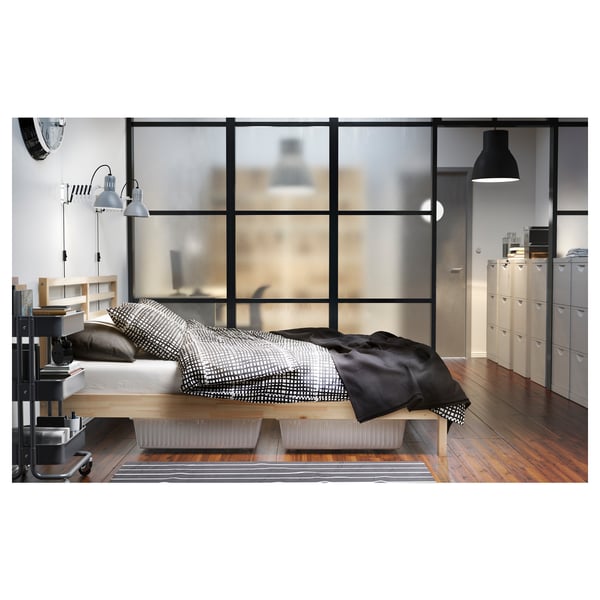 Modern bedroom featuring a light-colored wooden TARVA bed frame with a monochromatic bedding set against a large frosted window with wooden flooring.