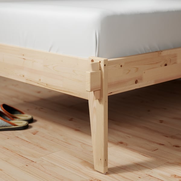 Wooden bed frame with light wood finish, featuring a simple and sturdy design, positioned on a wooden floor.