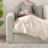 Person sitting on couch with blanket, holding cup.