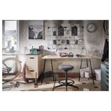 Industrial styled workspace with a desk, chair, and tools; concrete wall, clock, art.