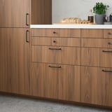 Modern kitchen with light brown TISTORP drawers and cabinets, sleek black handles, and white countertop featuring bread and plants.