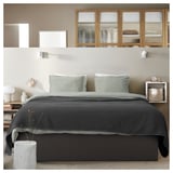 Modern bedroom with TJÅLLE gray bed frame featuring curved headboard, striped pillows, nightstands, and wall-mounted shelves.