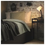 Cozy bed with striped pillows & gray blanket against brick wall, lit lamp on nightstand.
