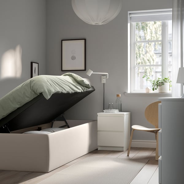 Minimalist bedroom with TJÅLLE storage bed, grey walls, white nightstand, light wood chair, and large window with sheer curtains.