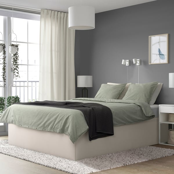 Modern bedroom with TJÅLLE bed, gray, upholstered, wide and low, beneath window, lamp, and decor.