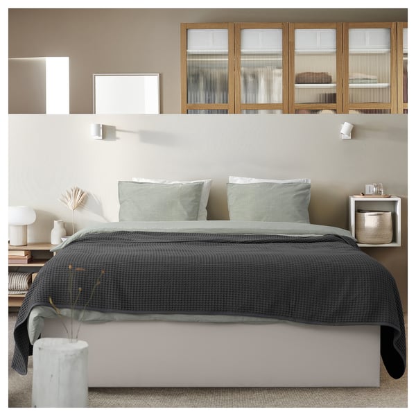 Minimalist bedroom with modern TJÅLLE bed in grey, featuring striped pillows, grey bedding, and sleek wooden nightstands with plants and lamps.