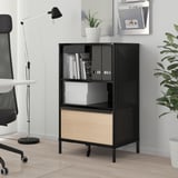 Black recycled paperboard TJENA magazine holder on desk with chair, lamp, plant, and houseplant. Slim, tall design with cut-out for easy access.