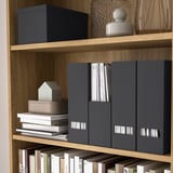 Wooden bookshelf with gray TJENA magazine holders organizing documents and books, displaying minimalist decor.
