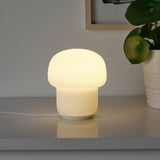 Small white mushroom-shaped lamp, glowing warm light, sits on a sleek grey surface. Its a cute, cozy ambiance creator.