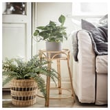 Rattan plant stand with woven basket and potted fern, near couch and door.