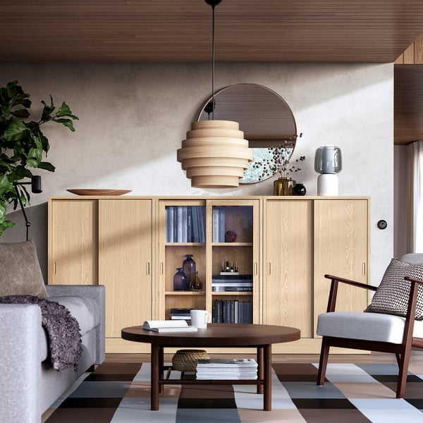 Modern living room with TONSTAD light wood cabinet, round mirror, unique pendant light, gray sofa, coffee table, striped rug, and armchair.