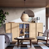 Modern living room with TONSTAD light wood cabinet, round mirror, unique pendant light, gray sofa, coffee table, striped rug, and armchair.