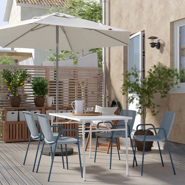 Modern patio set with white TORPARÖ table, four matching blue chairs, large beige umbrella, plants, and wooden privacy fence.