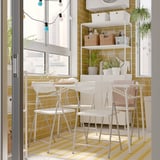 Bright balcony with white TORPARÖ table and chairs, yellow tiles, hanging lights, and potted plants.