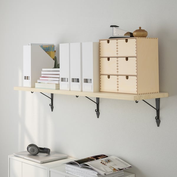 Wooden wall shelf holding boxes and books, with a light wood finish and black metal brackets. Display items include headphones and a vase.