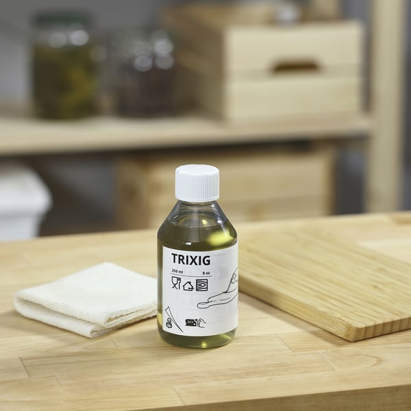 Green TRIXIG bottle on wooden table with cloth and board.